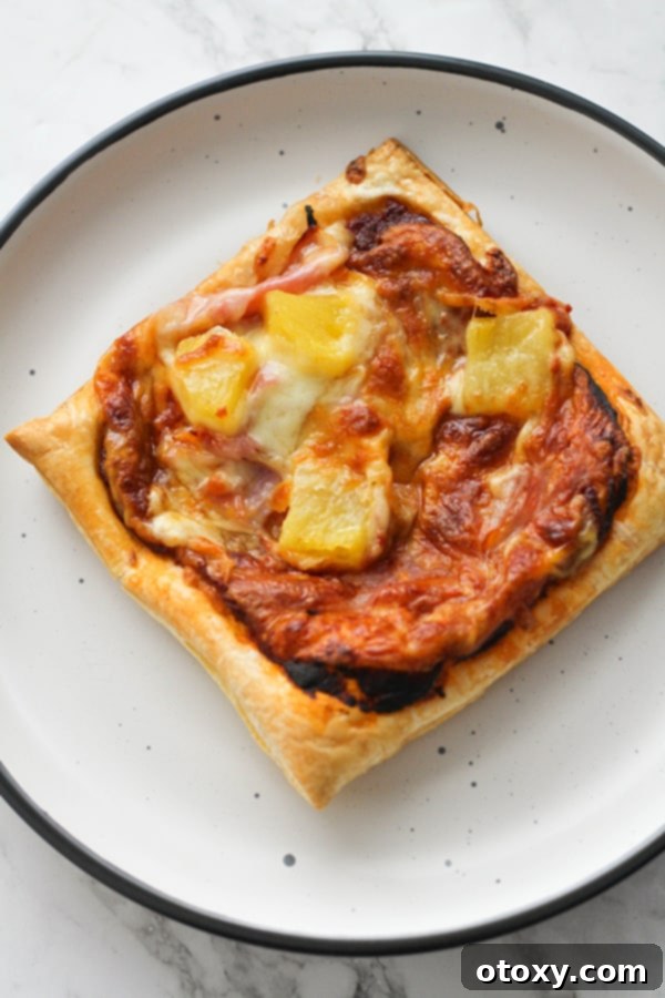 A perfectly baked puff pastry pizza slice on a white plate, showcasing its golden crust and melted cheese.