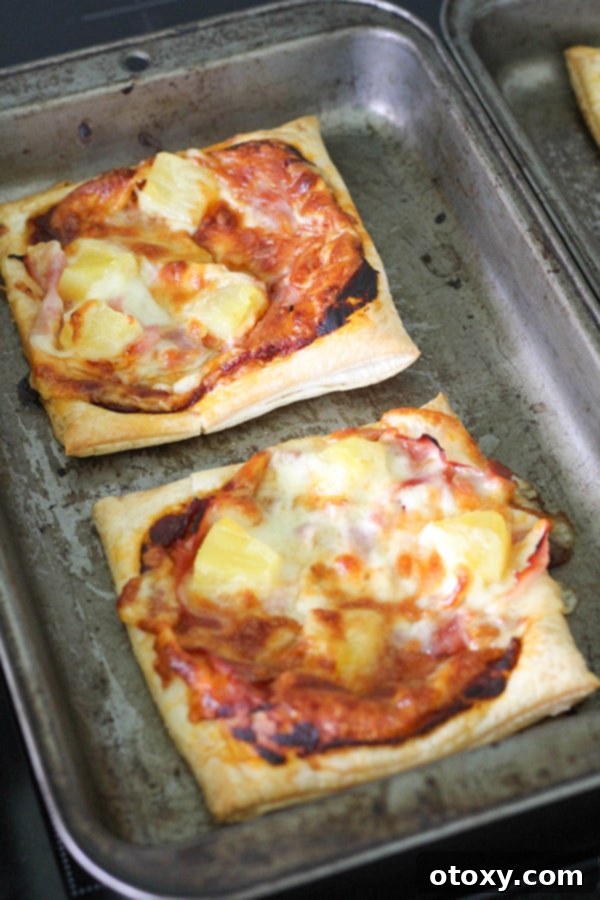 Puff pastry pizzas baking on a tray in the oven, showing their rising crusts.