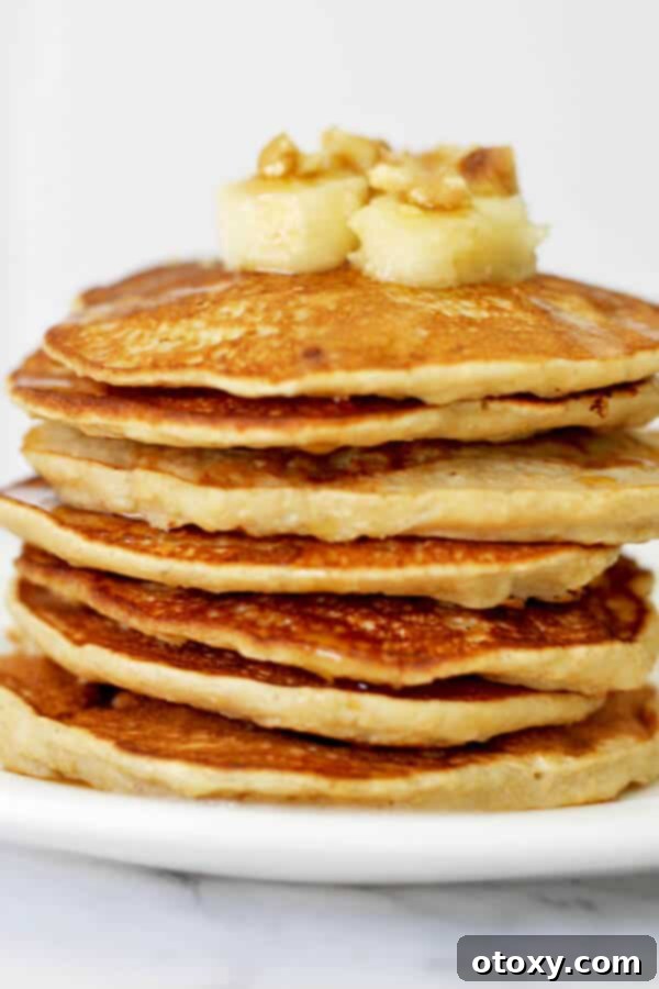stack of healthy banana pancakes on a white plate with caramelized banana slices and pecans on top