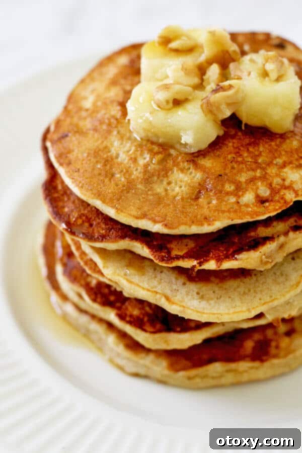 healthy banana pancakes stacked on a white plate with caramelized banana slices and pecans on top