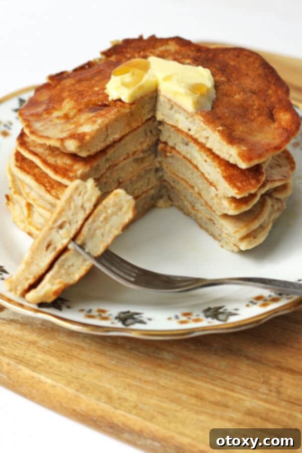 healthy banana pancakes layered on a patterned plate with a wedge sliced off to show the inside of the pancakes, revealing their fluffy texture