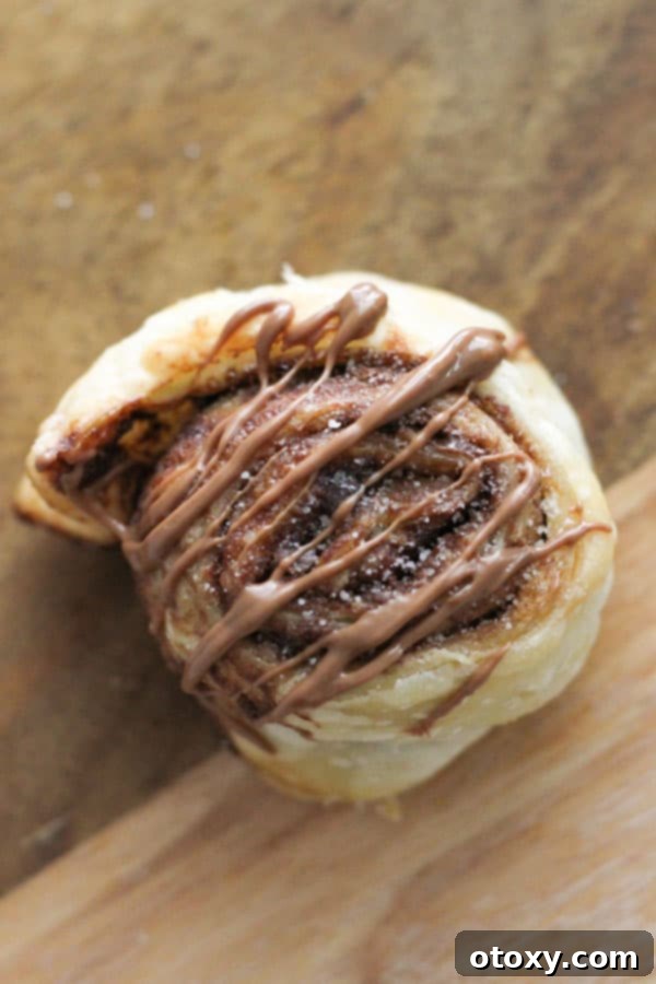 Chocolate Nutella Swirl Pastries Baked or Air Fried 3 a single chocolate pinwheel drizzled with chocolate, resting on a rustic wooden board.