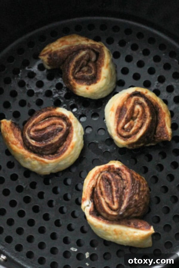 Chocolate Nutella Swirl Pastries Baked or Air Fried 10 golden brown pinwheels cooking inside an air fryer basket.
