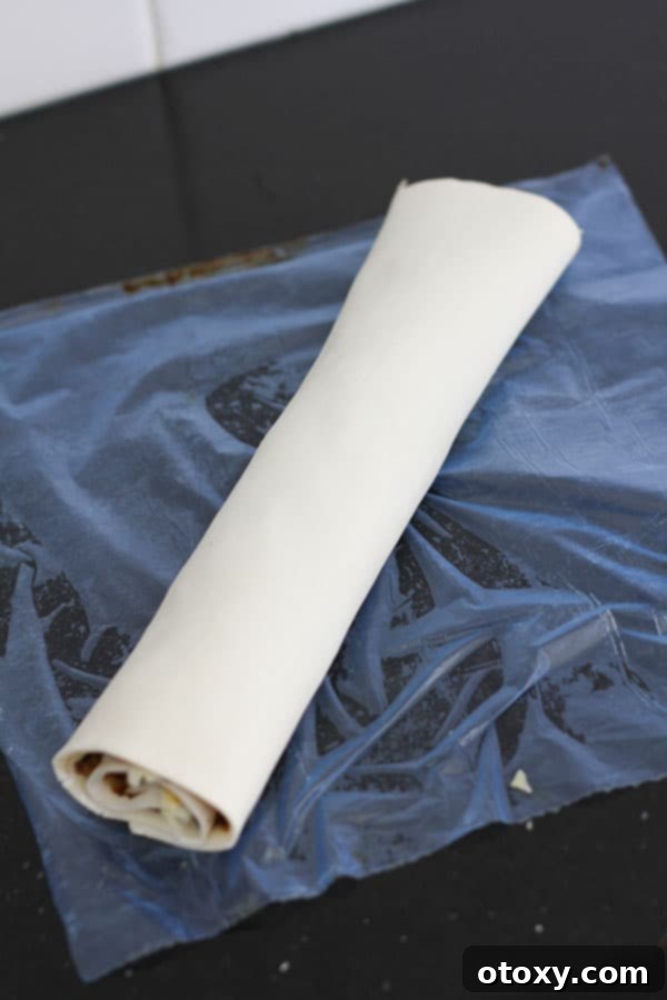 Easy Vegemite and Cheese Pinwheels Baked or Air Fried 6 Puff pastry tightly rolled into a uniform log after being spread with Vegemite and cheese, ready for slicing.