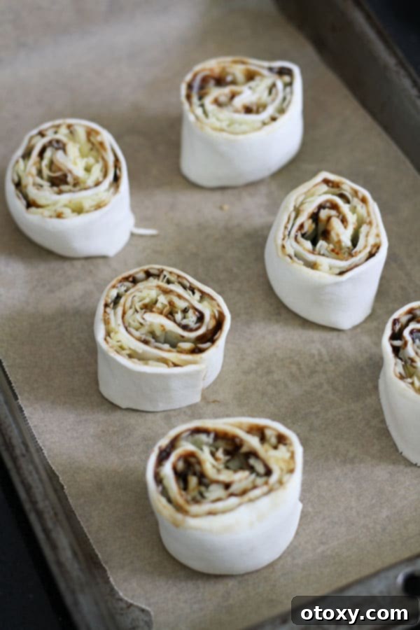 Easy Vegemite and Cheese Pinwheels Baked or Air Fried 7 Unbaked Vegemite and cheese pinwheel slices neatly arranged on a baking tray lined with parchment paper, ready for the oven.