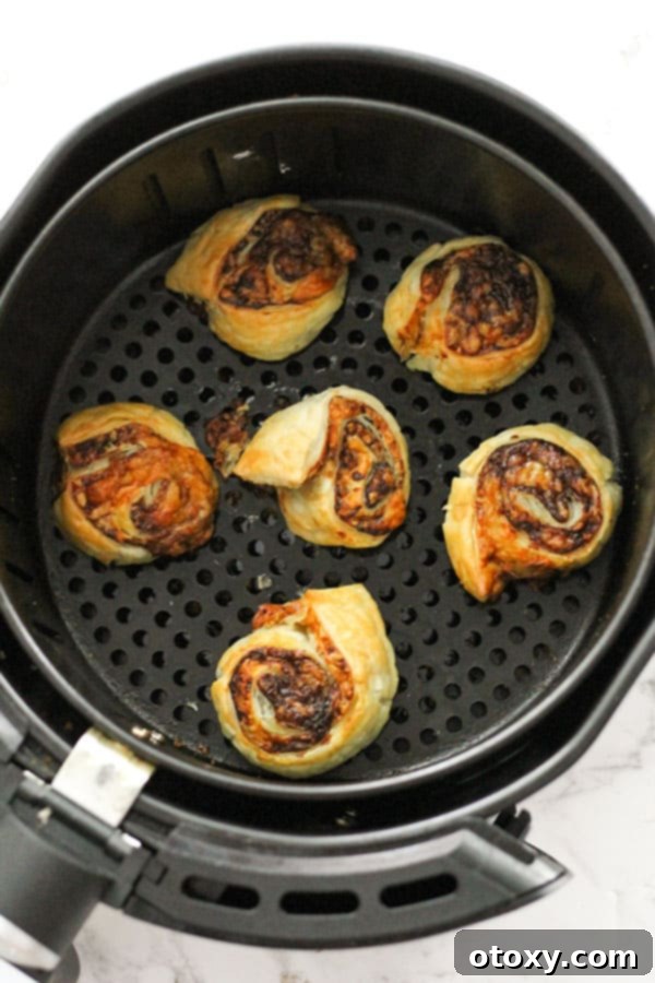 Easy Vegemite and Cheese Pinwheels Baked or Air Fried 9 Vegemite and cheese pinwheels cooking in an air fryer basket, with some space between each for optimal crisping.