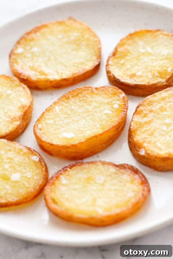 A vibrant close-up of crispy salt and vinegar potatoes, golden and textured, on a simple white plate.