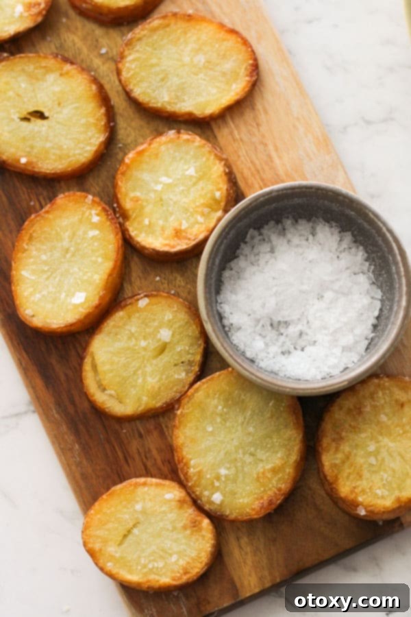 A rustic wooden serving board piled high with freshly roasted crispy salt and vinegar potatoes.
