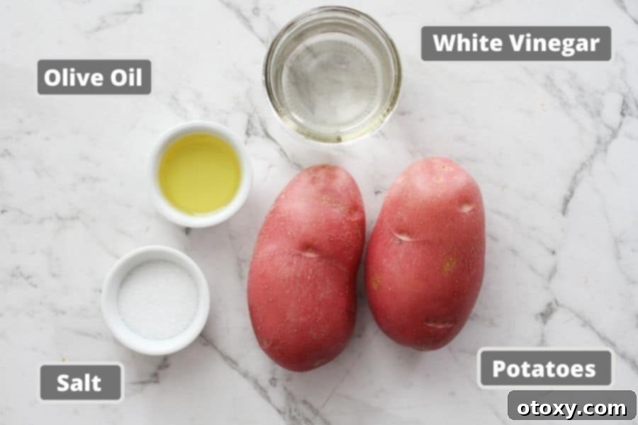 All the fresh ingredients for salt and vinegar potatoes laid out on a white marble background, including potatoes, white vinegar, olive oil, and salt.