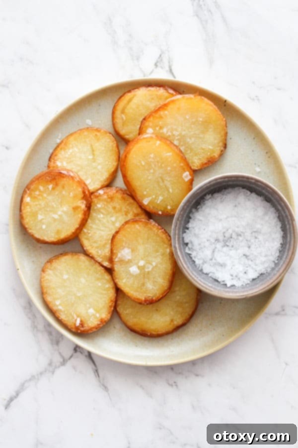 A serving of crispy salt and vinegar potatoes on a white plate, with a small bowl of salt for additional seasoning, ready to enjoy.