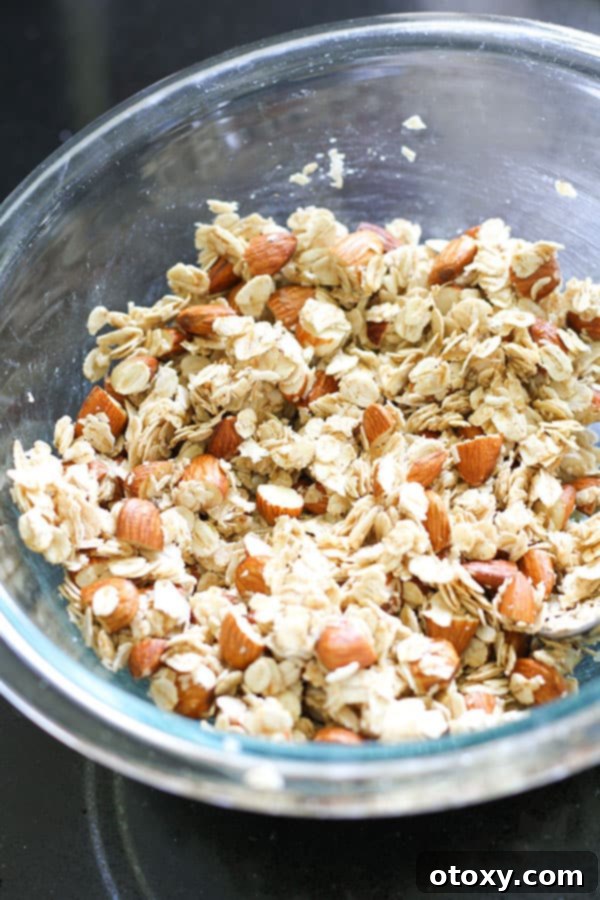 Granola ingredients thoroughly mixed in a clear glass bowl, showcasing the even coating of wet and dry components.