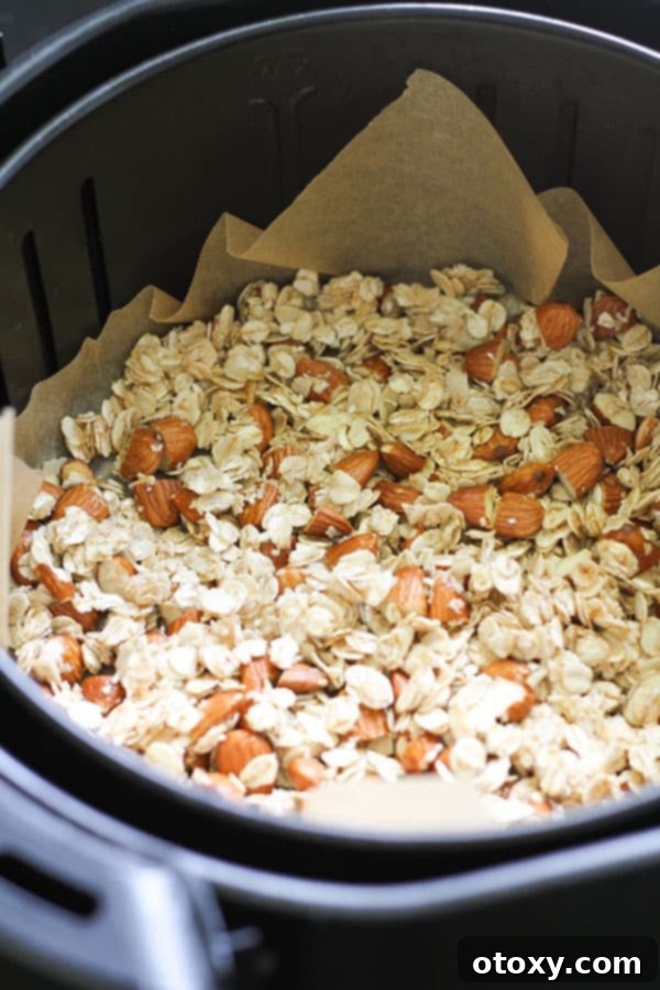 Raw granola mixture spread evenly on parchment paper inside an air fryer basket, perfectly ready for cooking.
