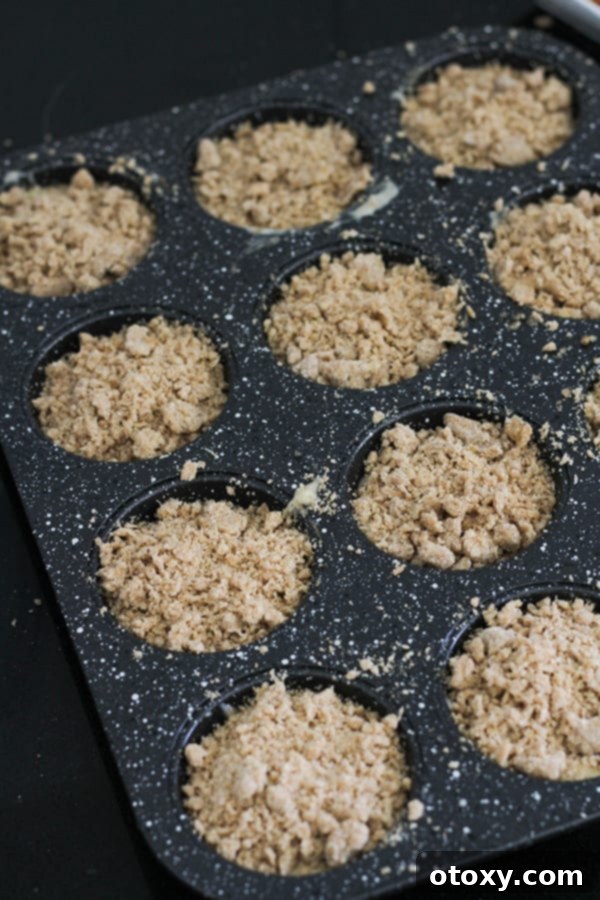 Muffin mixture in a muffin tray, now generously topped with the crumb mixture, ready for baking.