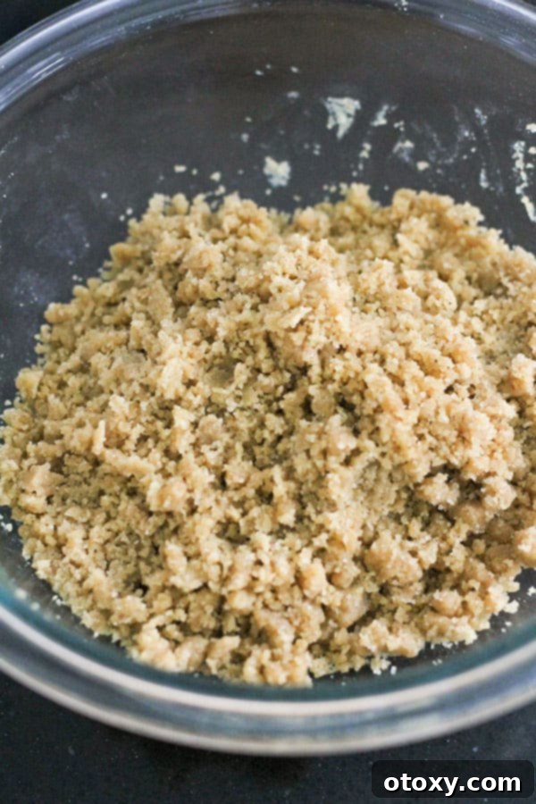 The crumb mixture, resembling wet sand, sits in a glass bowl, ready to be sprinkled over the muffin batter.