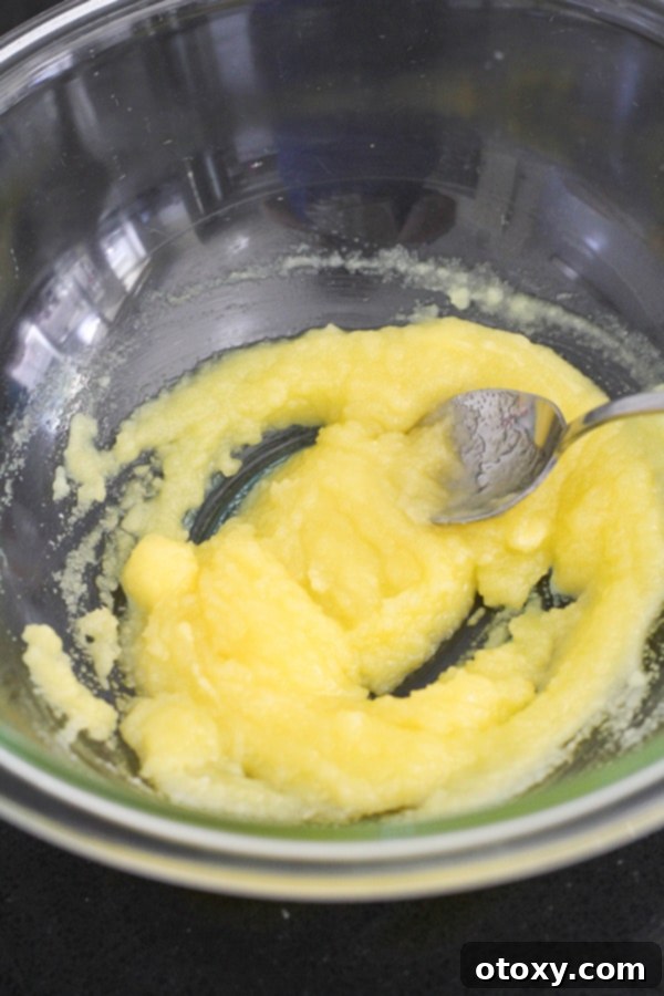 Melted butter and caster sugar are thoroughly mixed in a glass bowl, forming the base of the muffin batter.