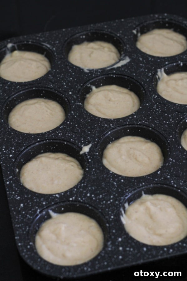 Muffin mixture neatly spooned into a 12-cup muffin pan, filling each cavity almost to the brim.