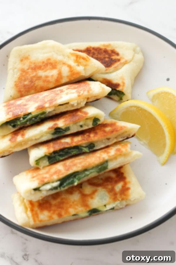 Stacked crispy golden Spinach and Feta Gozleme on a white plate, garnished with fresh herbs and lemon wedges, ready to be enjoyed.