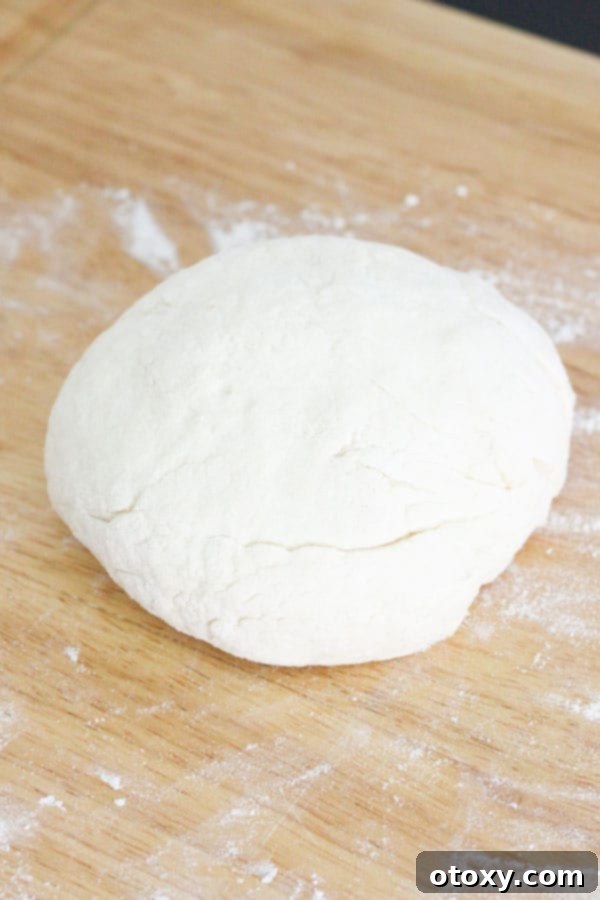 Freshly kneaded two-ingredient dough resting as a smooth, round ball on a wooden board, ready for the next step.