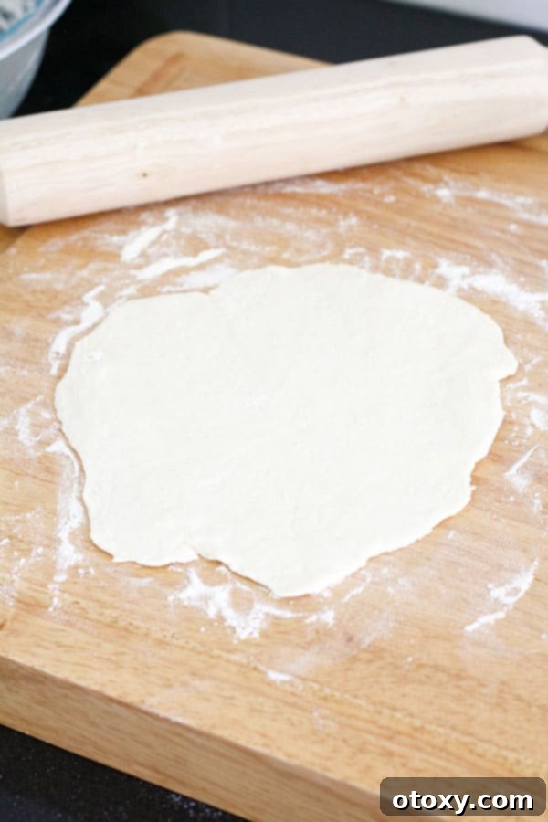 Thinly rolled out two-ingredient dough circle on a wooden board, perfectly prepared for its delicious filling.