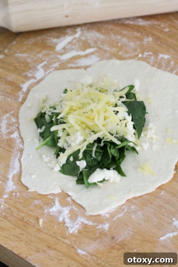 Two-ingredient dough half-filled with a generous and colorful mixture of fresh spinach, crumbled feta, and grated cheddar cheese.