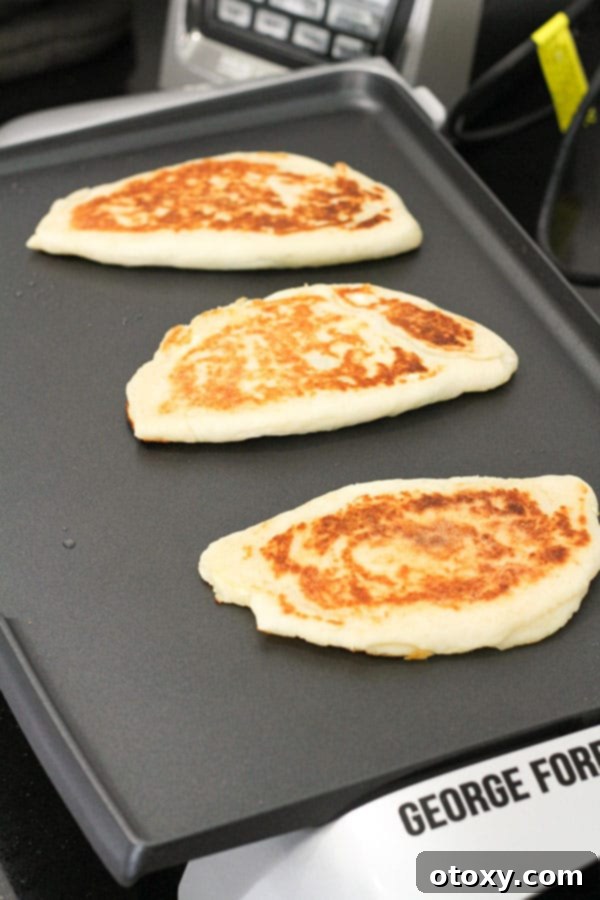 Spinach and Feta Gozleme sizzling and turning golden on an electric griddle, being pressed down with a spatula for even cooking.