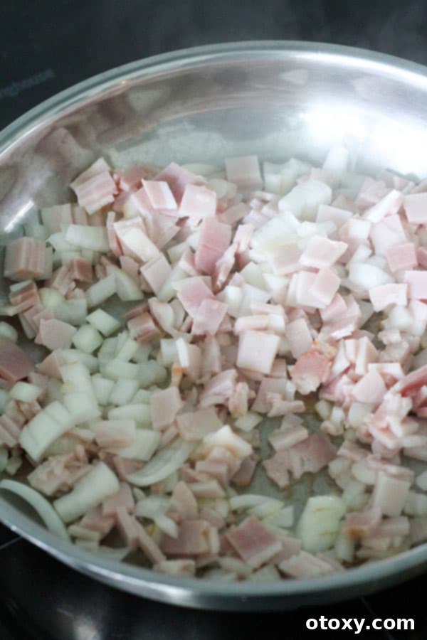 Diced bacon and sliced onion sizzling and cooking together in a frying pan over medium heat.