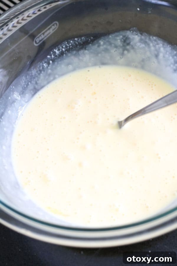 Close-up of whisked eggs and cream mixture in a clear glass bowl, seasoned with salt and pepper.