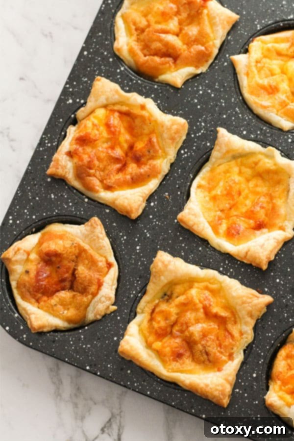 Baked mini egg and bacon pies, golden brown and puffed, cooling in a muffin tray.