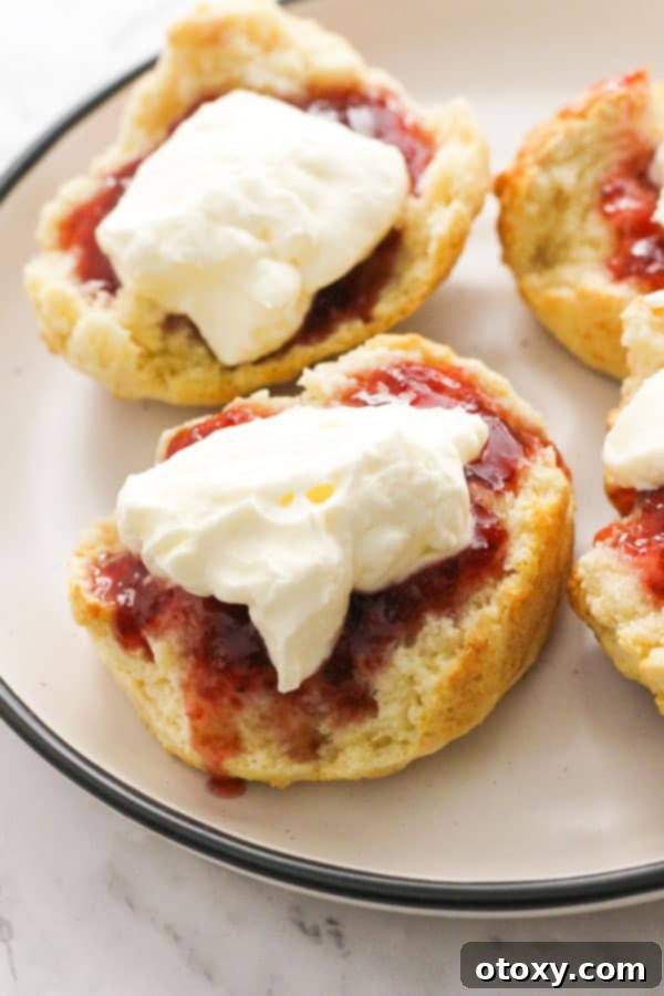 Golden Air Fryer Scones 2 A freshly baked air fryer scone, generously topped with vibrant red jam and a swirl of white cream, presented elegantly on a white plate, ready to be enjoyed.