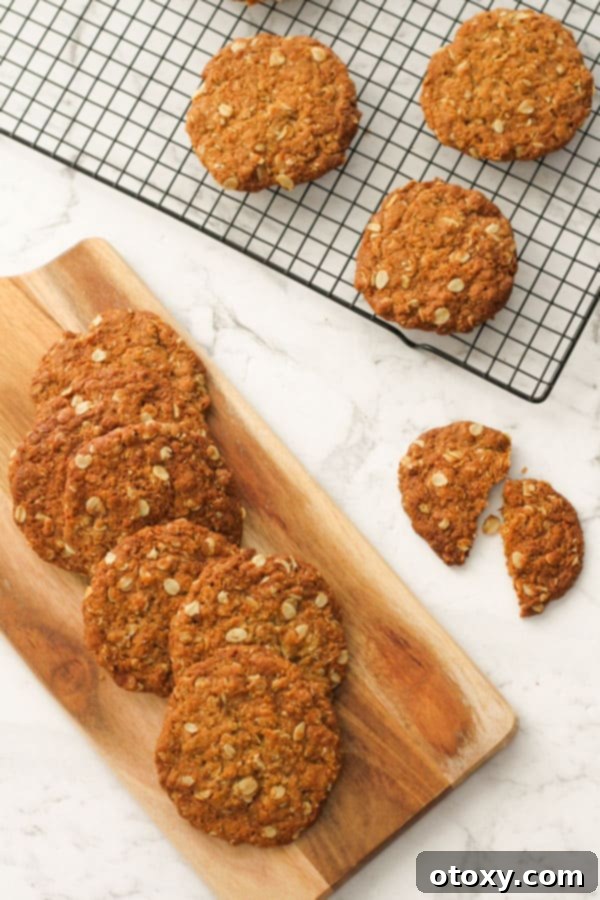 Golden brown Anzac biscuits arranged beautifully on a rustic serving board and a cooling wire rack, highlighting their perfect crunchy texture.
