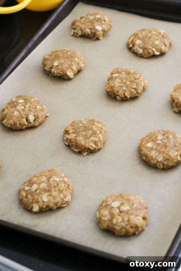Neatly arranged, uncooked Anzac biscuits await their transformation on a baking tray lined with parchment paper.