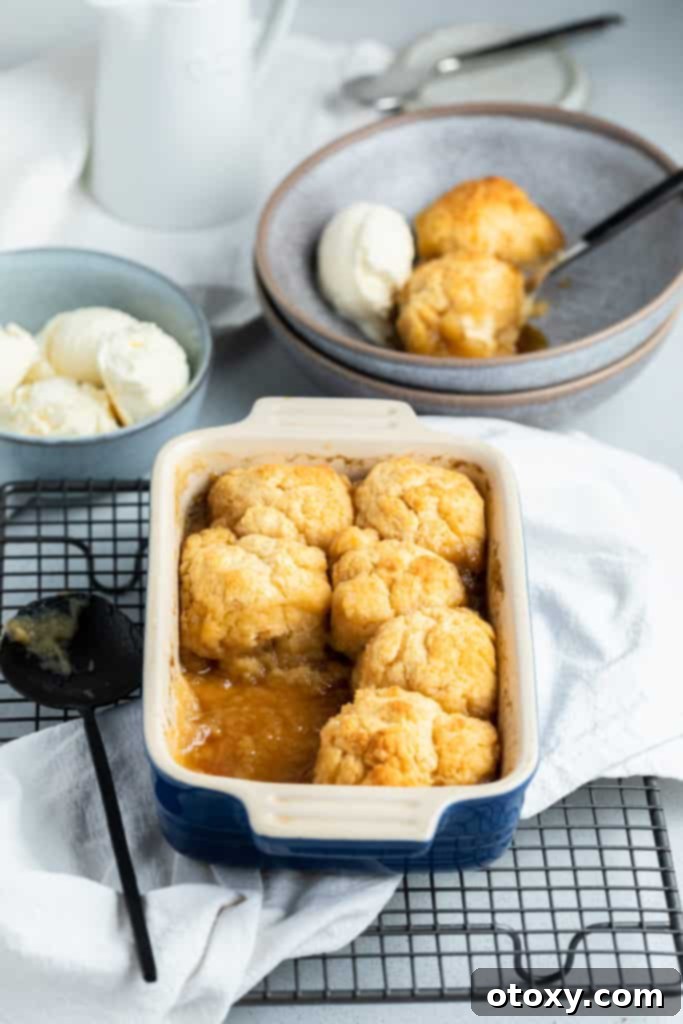 golden syrup dumplings in a baking dish on top of a wire tray with a bowl of ice cream in the background.