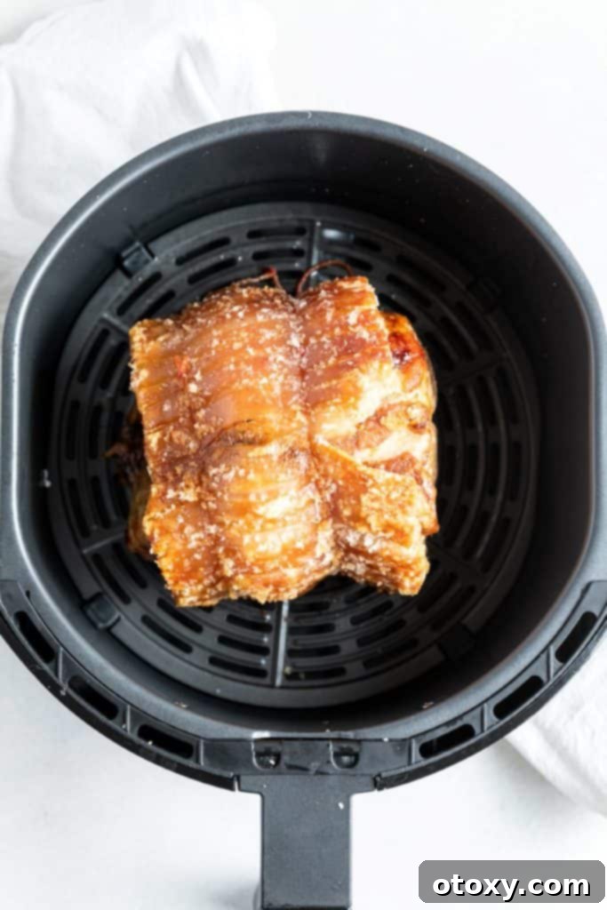 Fully cooked roast pork in an air fryer basket, with perfectly golden and crispy crackling.