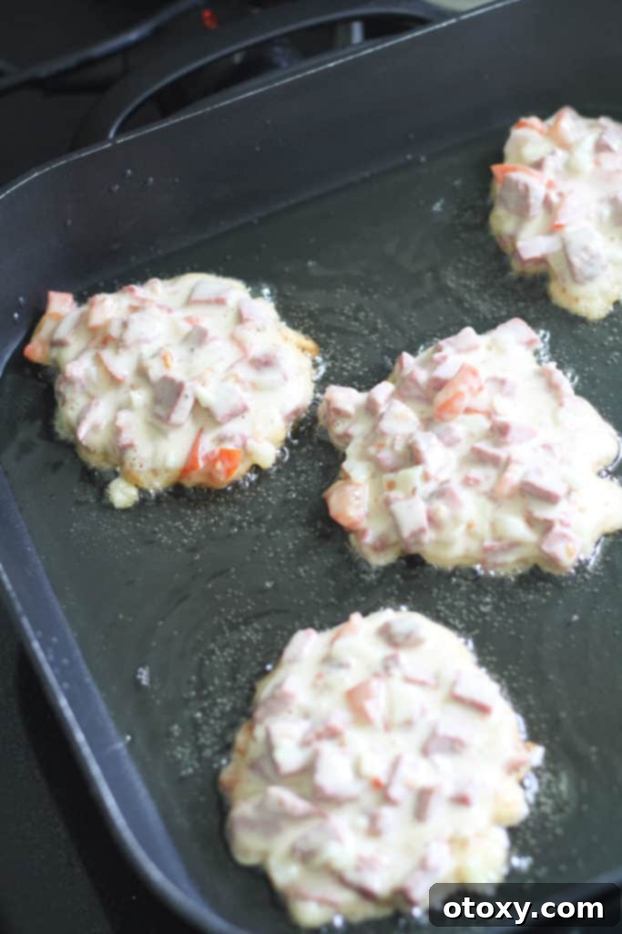 Multiple corned beef fritters shallow frying in a hot pan, sizzling to a golden crisp.