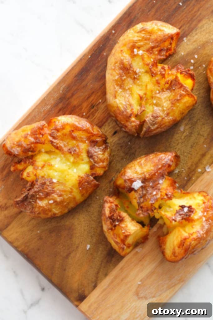Three perfectly crispy air fryer smashed potatoes arranged artfully on a rustic wooden board.