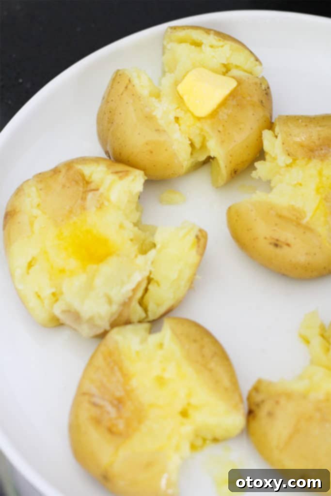 Boiled and smashed potatoes on a white plate, topped with small chunks of butter and a sprinkle of sea salt.