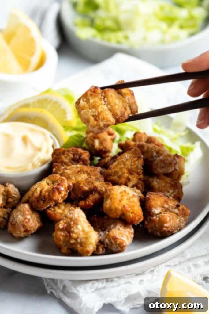 Golden Crispy Air Fryer Karaage 8 a chopstick holding a piece of karaage chicken in the air above a plate of karaage.