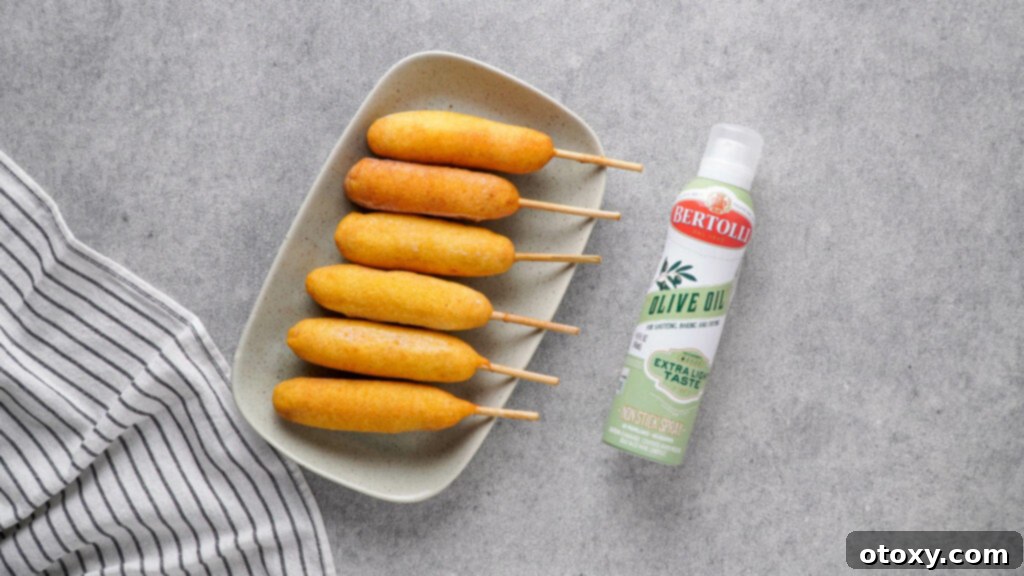 Frozen corn dogs and olive oil spray on a grey plate, ready for air frying