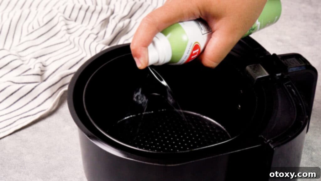 Spraying cooking oil onto an air fryer basket before adding corn dogs