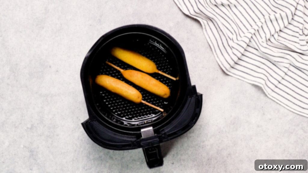 Top shot of air fryer basket with frozen corn dogs placed in a single, even layer