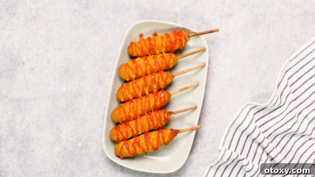 Finished air fryer corn dogs with ketchup and mustard on a grey plate, ready to be served