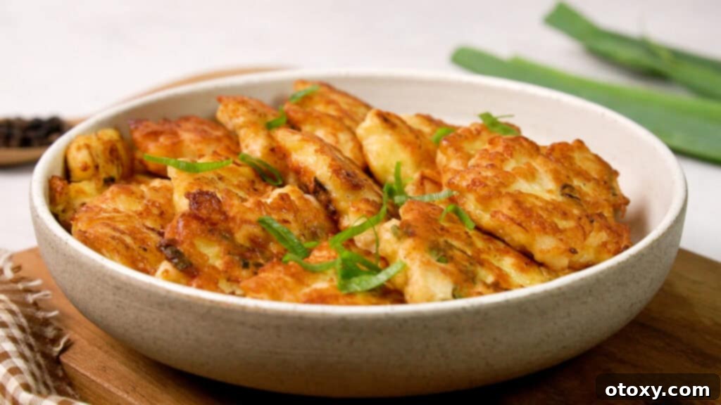 Crispy Chicken Delights 12 A stack of freshly cooked chicken fritters on a white plate, garnished with finely chopped spring onions, ready to be served.