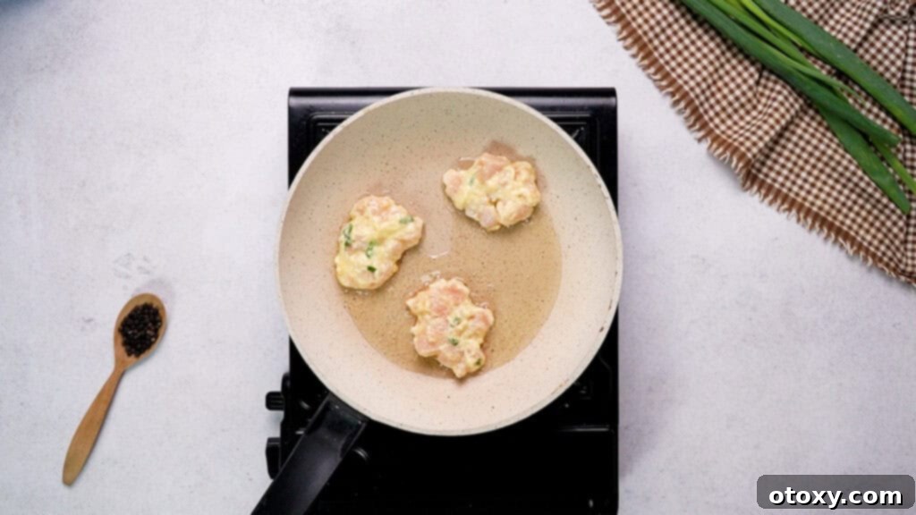 Crispy Chicken Delights 10 Several scoops of chicken fritter mixture cooking in hot olive oil in a non-stick pan, spaced evenly.