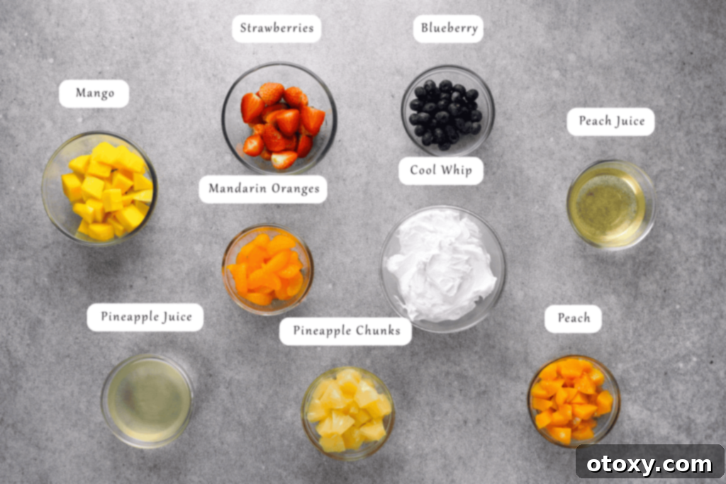 All the ingredients for the fruit salad with Cool Whip laid out on a kitchen counter: Cool Whip, canned pineapple chunks, mandarin oranges, peach halves, mango, strawberries, and blueberries.