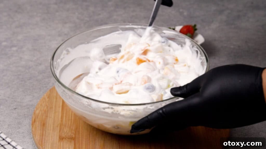 Step 4: Stirring the fruit and Cool Whip mixture gently with a large spoon.