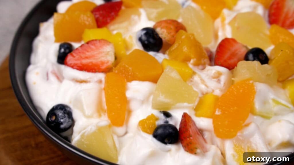 Step 6: The finished fruit salad with Cool Whip, served in a glass bowl with a spoon, ready to be enjoyed.