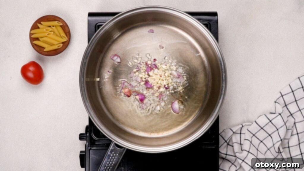 Shallots and minced garlic being stir-fried in olive oil in a frying pan.