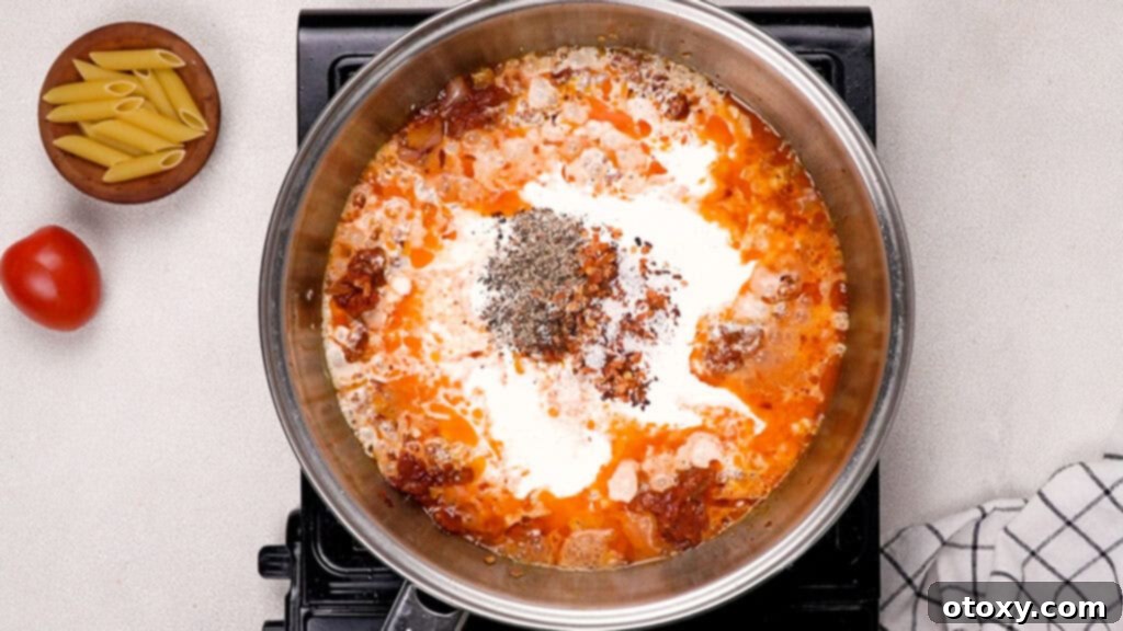 Heavy cream, chili flakes, salt, and black pepper being stirred into the tomato paste mixture in a frying pan.