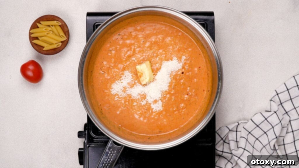 Freshly grated Parmesan cheese and butter being added to the simmering cream and tomato sauce.