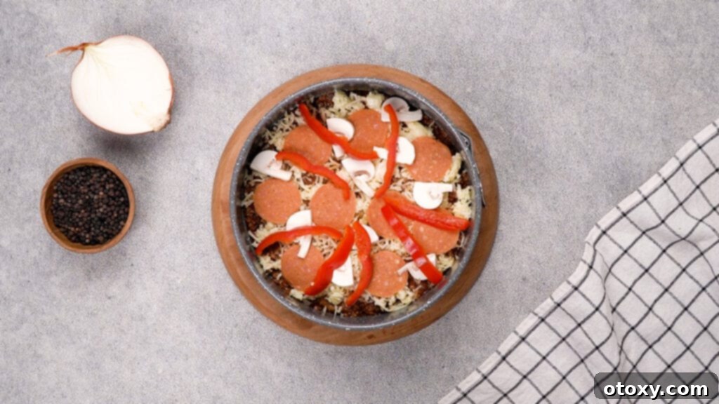 Shredded mozzarella cheese, pepperoni, mushrooms, and red bell pepper layered on top of the beef base in a baking pan.